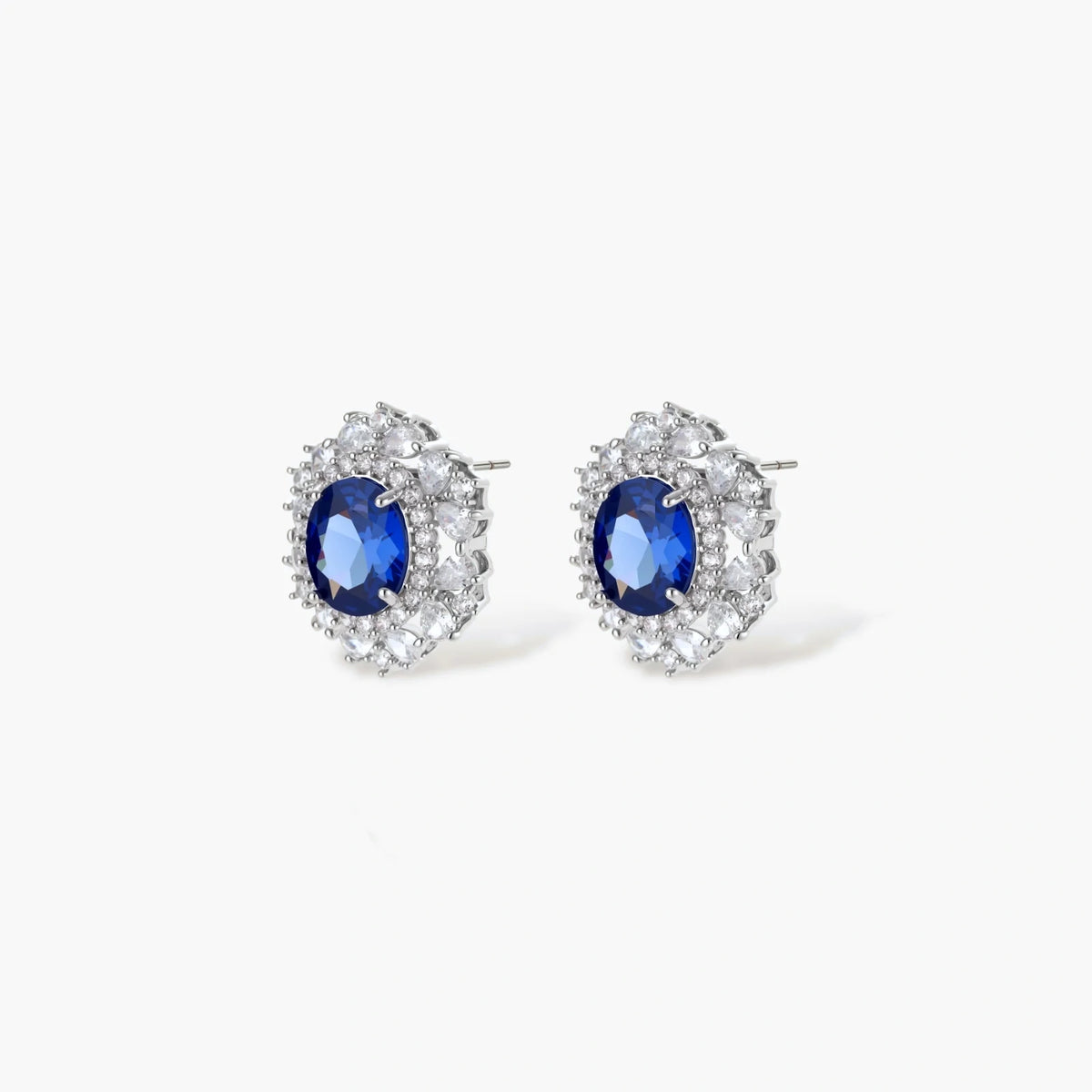 White gold plated jewelry set with blue cubic zirconia centers surrounded by clear crystal halos on cream background.