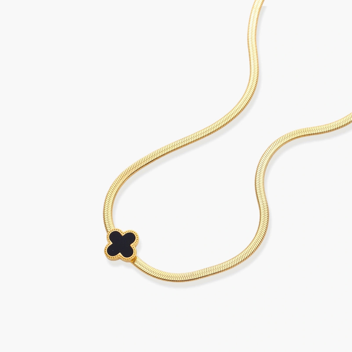 Dainty 18K gold-plated herringbone chain necklace with black enamel quatrefoil clover pendant on white background