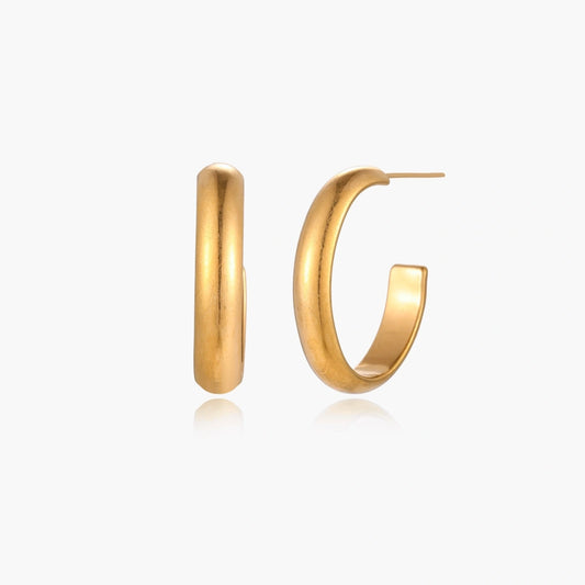 Chunky tubular hoop earrings in warm 14K gold-plated finish with smooth polished surface on cream background.