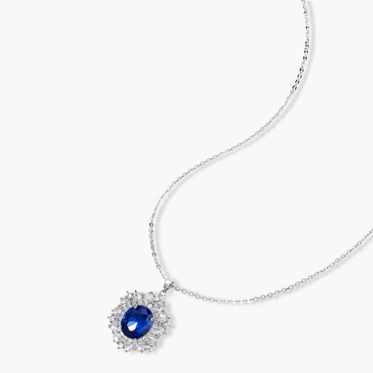 White gold plated jewelry set with blue cubic zirconia centers surrounded by clear crystal halos on cream background.