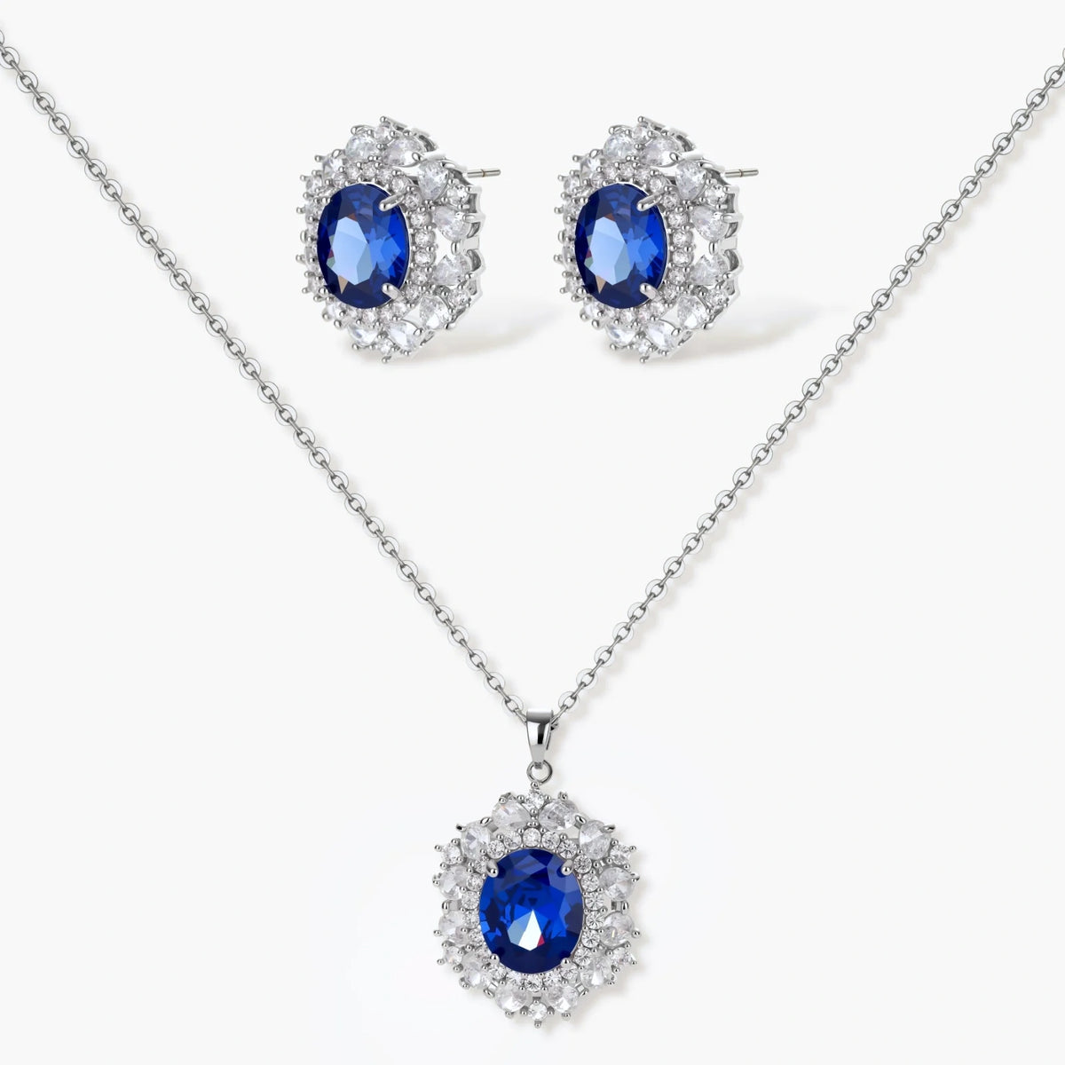 White gold plated jewelry set with blue cubic zirconia centers surrounded by clear crystal halos on cream background.