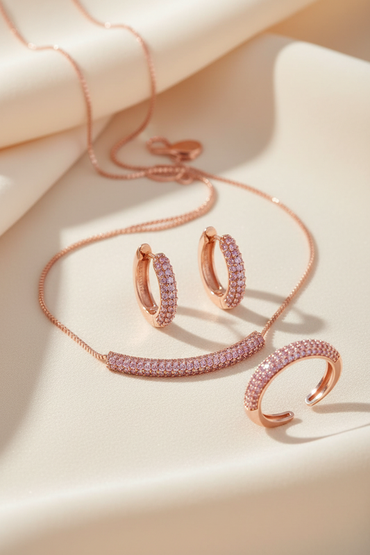 Conjunto de joias pavê rosa com colar, brincos de argola e anel ajustável sobre fundo marfim e rosa suave